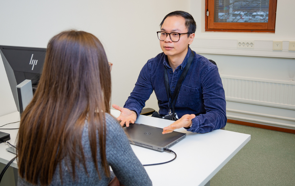 An employee advises a customer in an office, behind a desk and computer